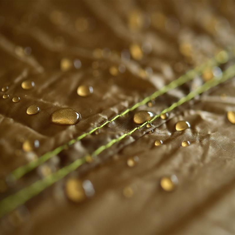 Close-up of water droplets on the Adventure Ultra-Light Tarp by Amazonas reveals the material's textured brown nylon ripstop fabric with green stitching, showcasing its excellent water-repellent properties, ideal for an ultra-light hammock.