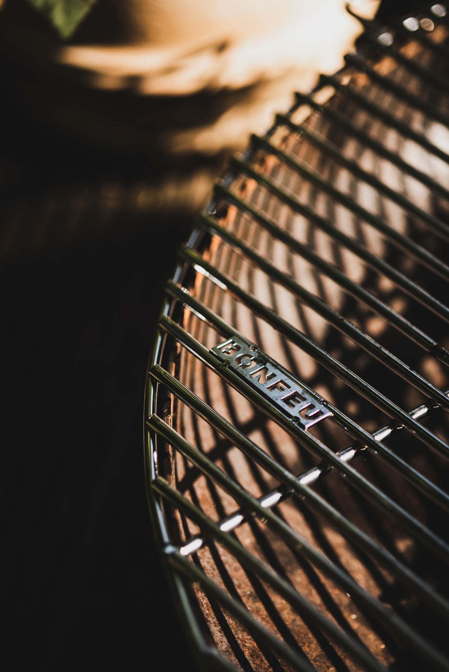 Close-up of a steel grate with the words "Bongrill full circle" embossed on the surface, captured under dramatic lighting. Shadows and highlights accentuate the curved lines, creating a dynamic and contrasting visual effect ideal for any barbecue enthusiast who appreciates Bonfeu's design.