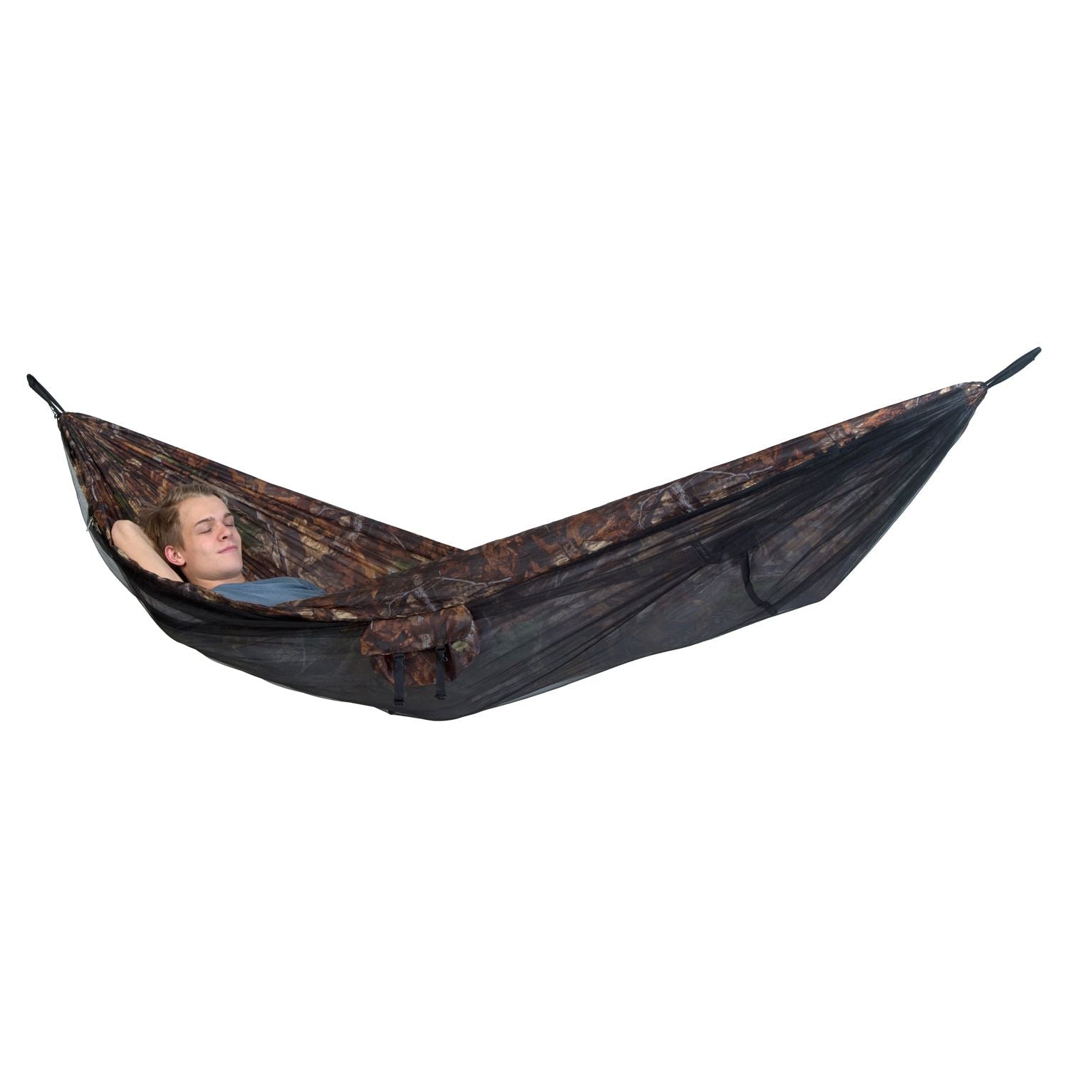 A person is comfortably lounging in the Moskito-Traveller Forest hammock by Amazonas, which features an ultralight design and a camouflage pattern with a built-in mosquito net. Suspended above the ground, they seem relaxed, resting with their head slightly propped up on a pillow and seamlessly blending into the forest environment.