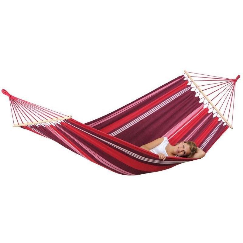 A person is peacefully relaxing on the Samba Fuego Hammock by Amazonas, featuring weather-resistant fabric with vibrant red and purple stripes. They are lying on their side with eyes closed, while the hammock is suspended securely by sturdy wooden spreader bars at each end against a plain white background.