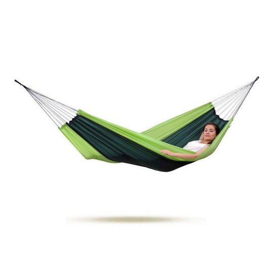 An individual lounging in an Amazonas Silk Traveller Forest Hammock, featuring a green and dark green Ripstop Nylon design, suspended mid-air against a plain white backdrop. This hammock is ideal for outdoor enthusiasts, offering a slightly curved shape that provides comfortable support for resting inside.