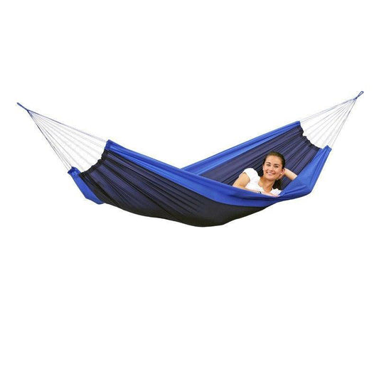 A person smiling and reclining comfortably in an Amazonas Silk Traveller Ocean Hammock, made from durable ripstop nylon and suspended with white ropes, while wearing a white shirt against a plain white background.