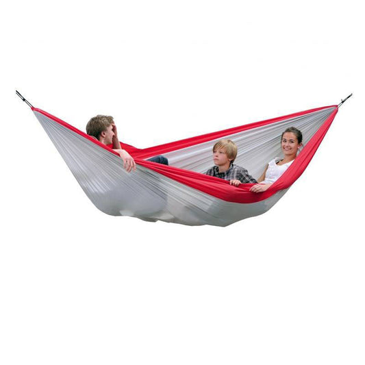 Three people sit comfortably in a spacious, red and white Silk Traveller XXL Hammock by Amazonas. Suspended in mid-air, this travel essential cradles the relaxed and cheerful group, highlighting its Ripstop Nylon durability.