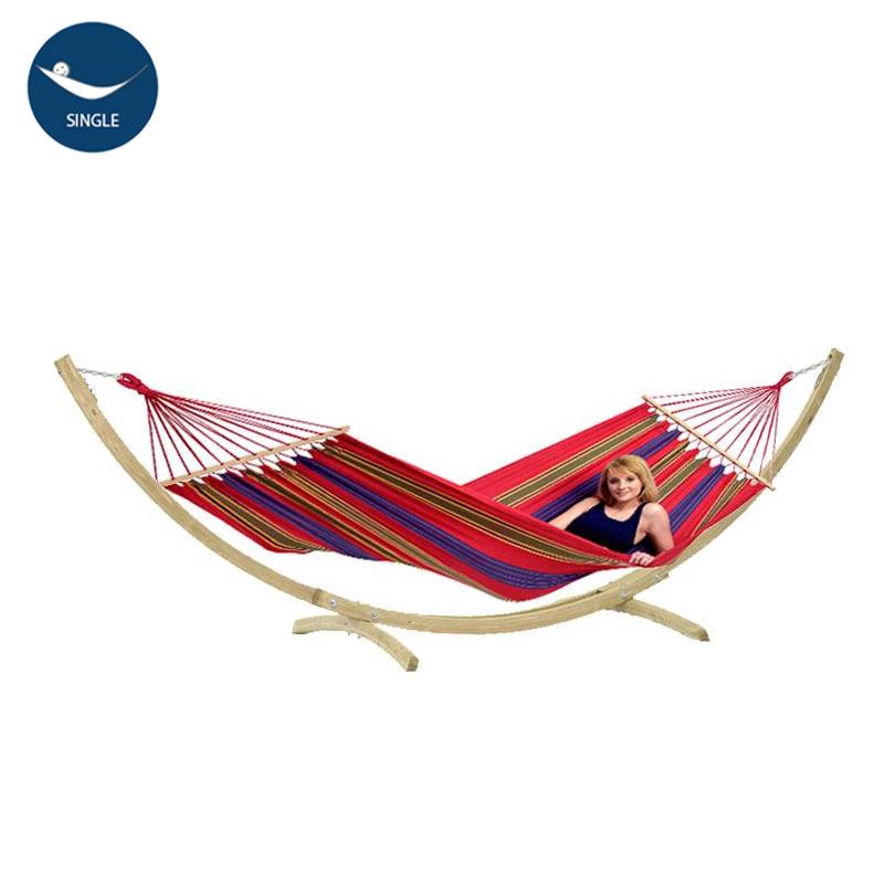 A person is reclining and smiling in the vibrant Star Hammock Set by Amazonas, which rests elegantly on a wooden stand. With its weatherproof design and designation for single use, this hammock adds a charming touch to any garden.