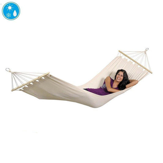 A woman in a purple shirt is lounging on an Amazonas Tobago Natura Hammock, smiling and enjoying her relaxation. The hammock boasts weather-resistant hardwood spreader bars on each end, floating comfortably in the air. The plain white backdrop is adorned with small icons representing temperature and water droplets.