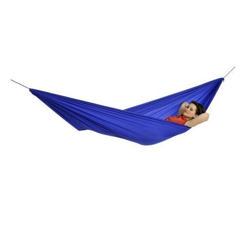 Wearing a red shirt, an outdoor enthusiast lounges in a durable Travel Hammock Set Blue by Amazonas, expertly crafted from ripstop nylon. The hammock offers a plush resting place, hanging against a plain white background that accentuates both the individual and their snug sanctuary.